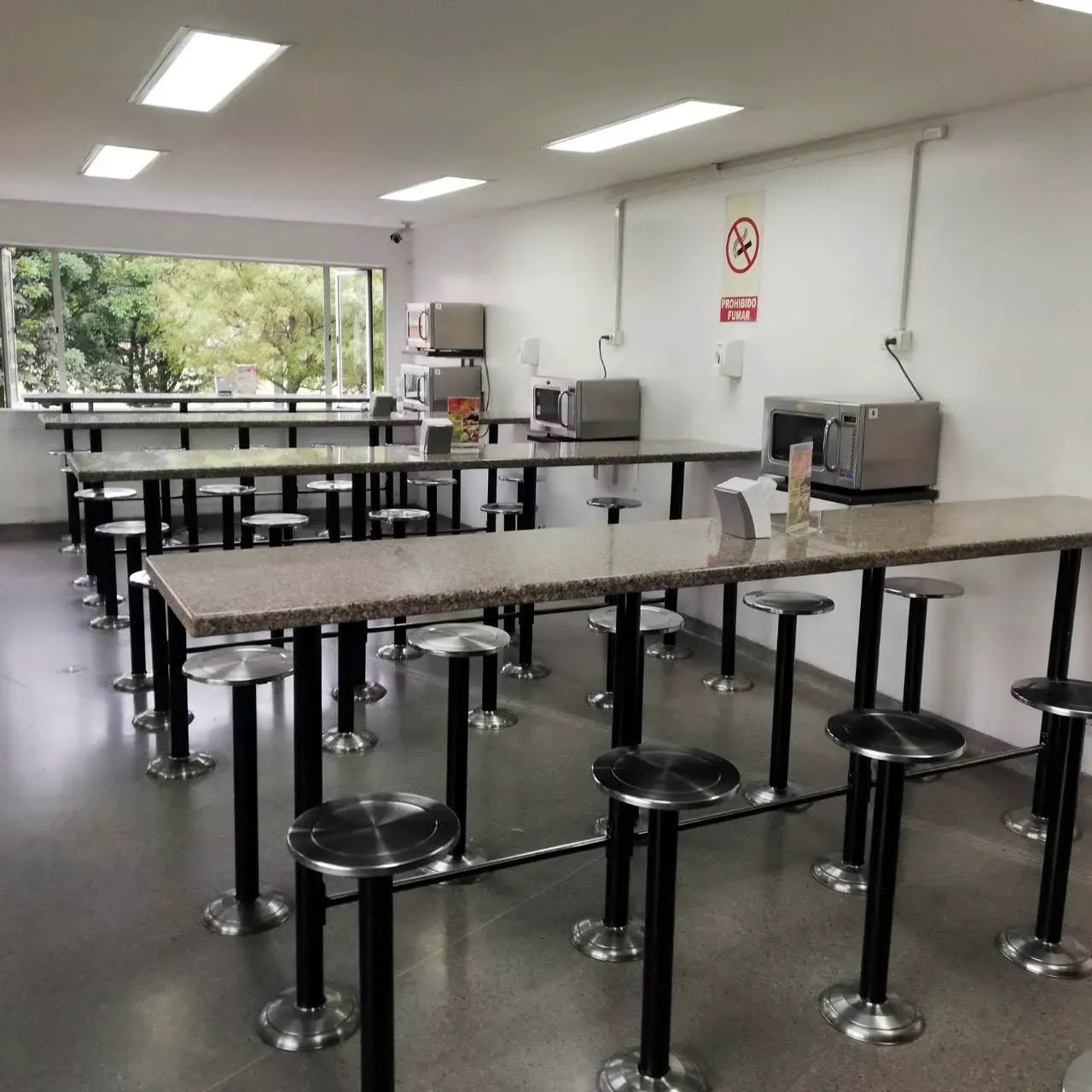 Comedor de empresa: Mesas altas con taburetes fijos al piso.